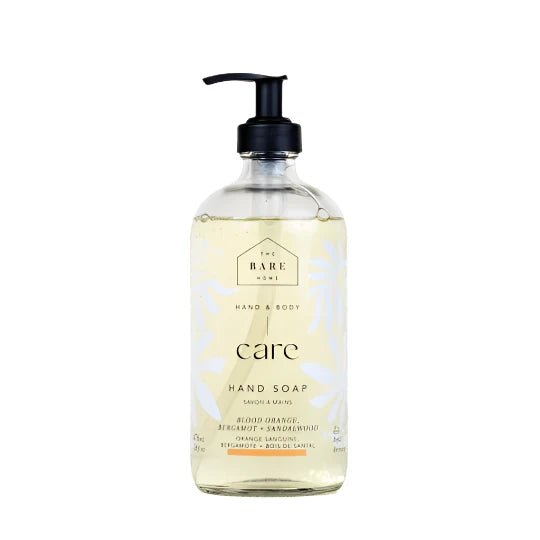 A clear glass pump bottle with a label that reads 'The Bare Home Hand Soap - Blood Orange, Bergamot & Sandalwood'. The liquid inside appears to be a light yellow or orange color, consistent with the blood orange and bergamot scents.