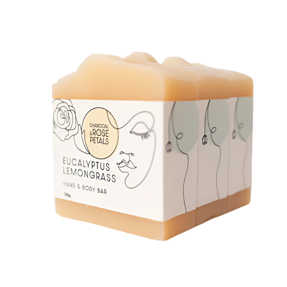 A stack of Charcoal and Rose Petals eucalyptus lemongrass soap bars. They have a slightly yellow hue and are wrapped in white labels.