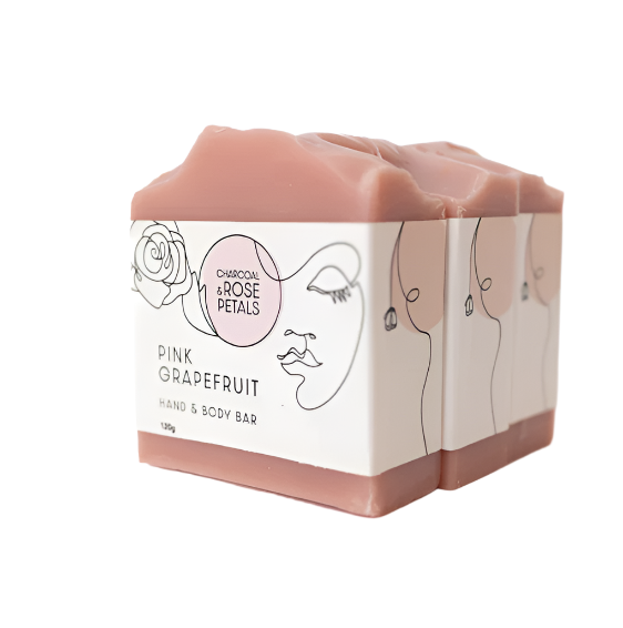 A bar of hand and body soap with 'Charcoal & Rose Petals' label, indicating the scent of pink grapefruit. The packaging is white with rose and face illustrations.