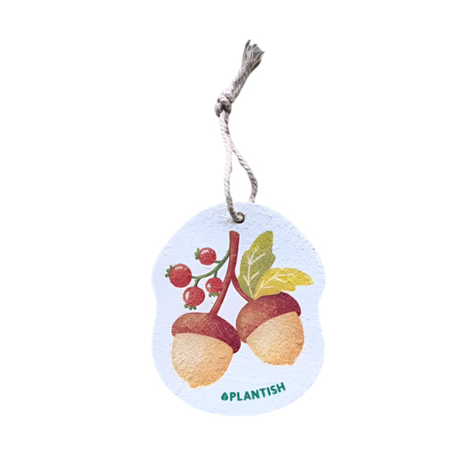 A white dish sponge with a printed design of acorns and leaves in brown and red colours, with a string attached to the top.