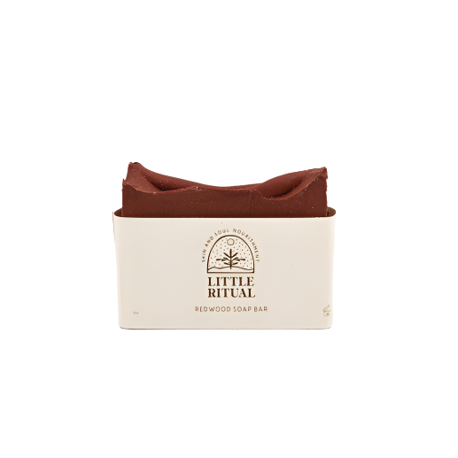 A red clay bar soap from Little Ritual with a beige label wrapped around it indicating it is the redwood soap bar.